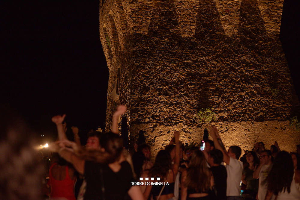 Crowd celebrating at night in front of the illuminated Torre Dominella tower